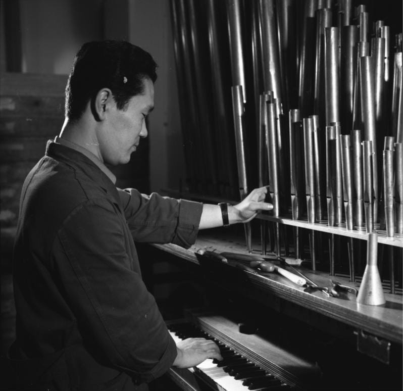 Archival black-and-white photo of an organ builder working among pipes in the Klais workshop in Bonn.
