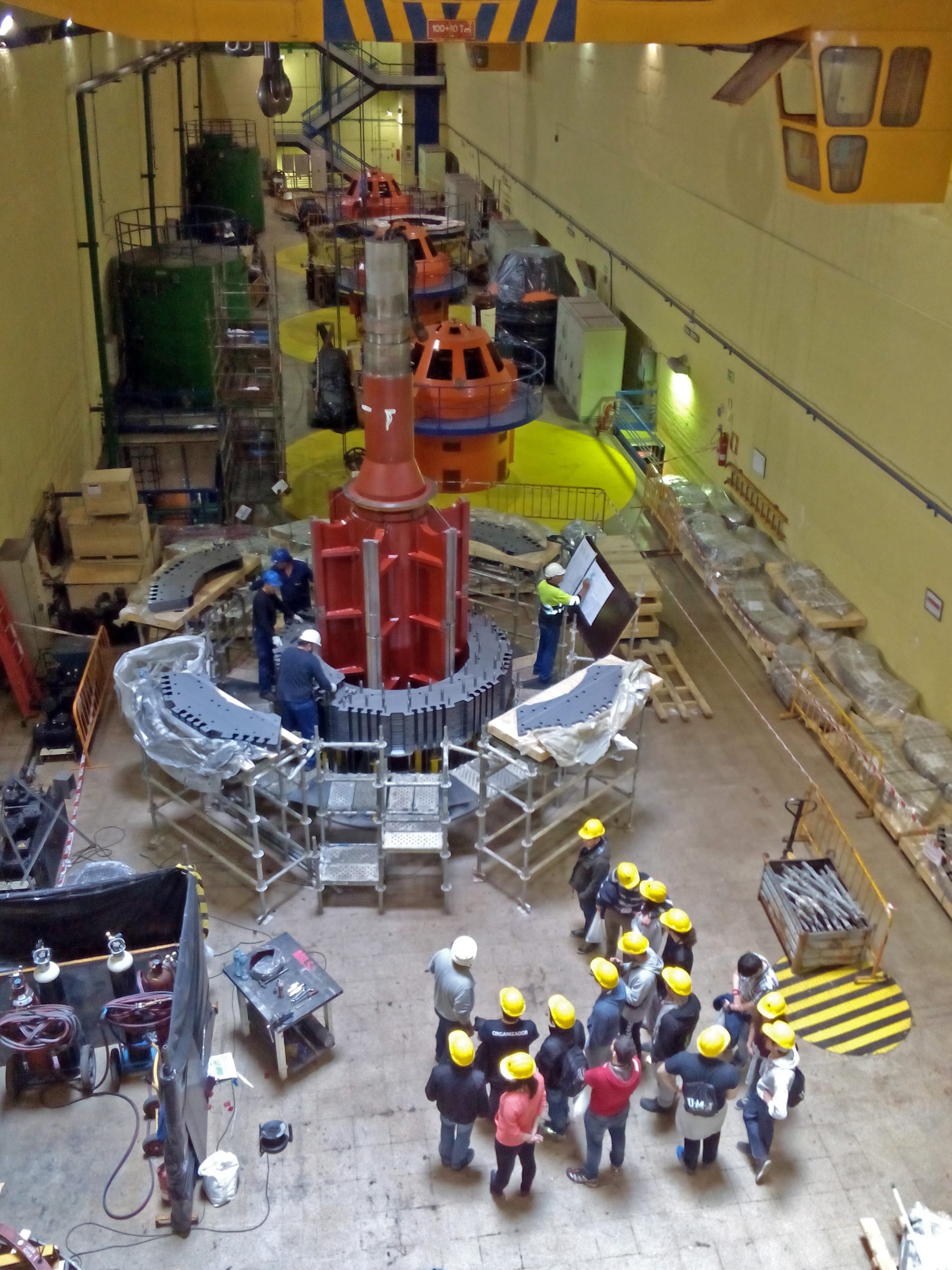 Engineers and technicians gathered around the exposed rotor of a large generator inside a power station hall.