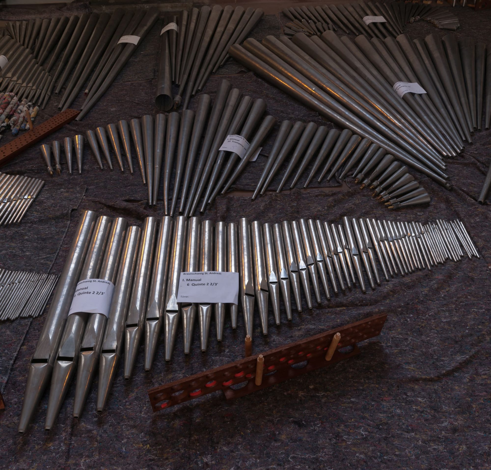 Disassembled organ pipes laid out on dark cloth during restoration work, sorted by size and rank.