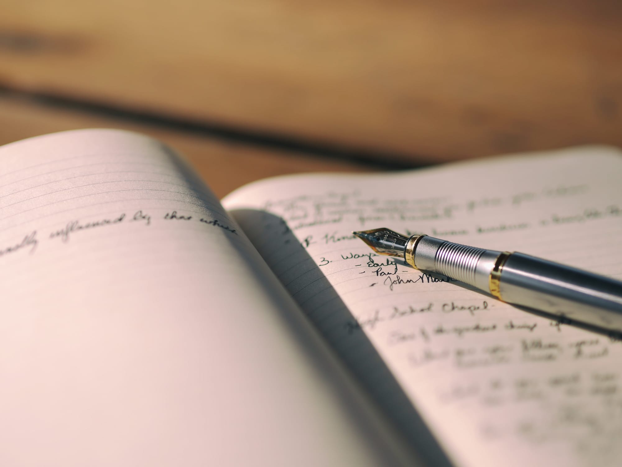 An open handwritten journal with a fountain pen lying diagonally across the pages.