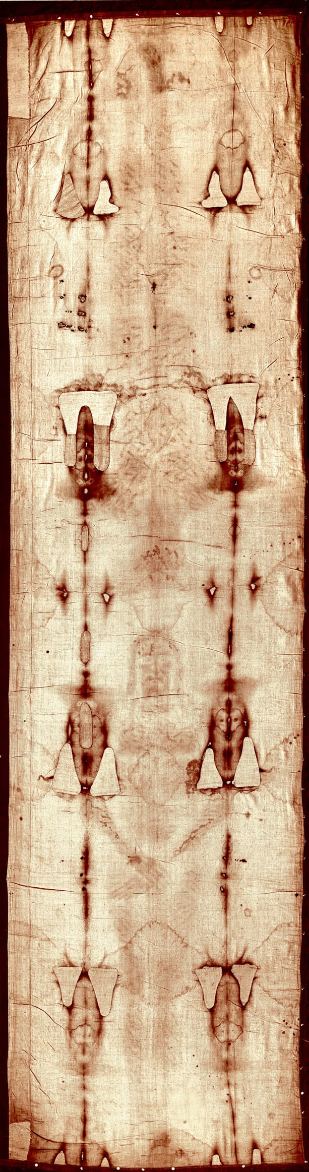 Full-length photograph of the Shroud of Turin showing faint markings of a human form as a narrow vertical strip of aged linen cloth
