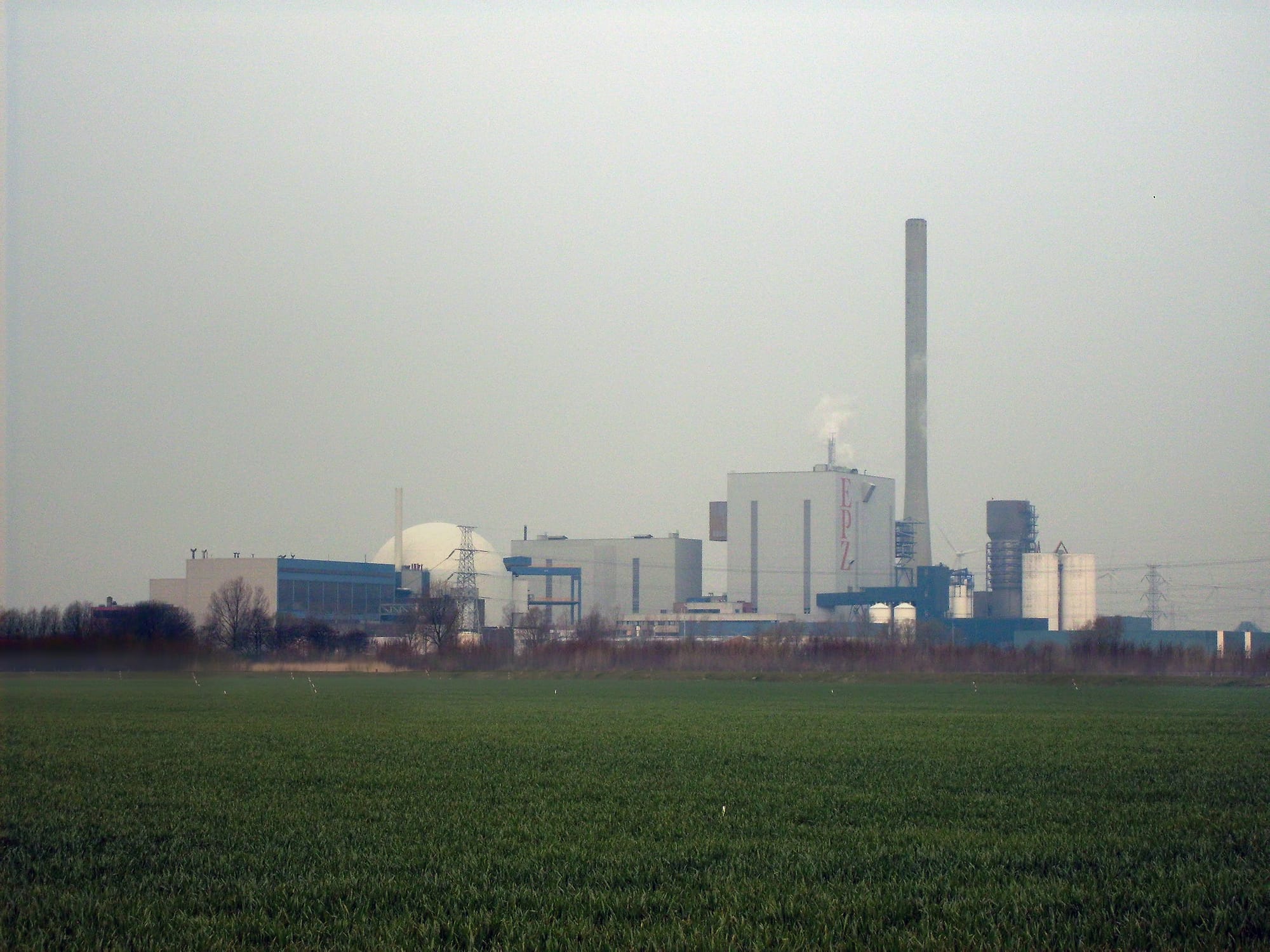 Kerncentrale Borssele met witte koeltorens en cilindrisch reactorgebouw langs een kanaal, omgeven door Zeeuws polderlandschap
