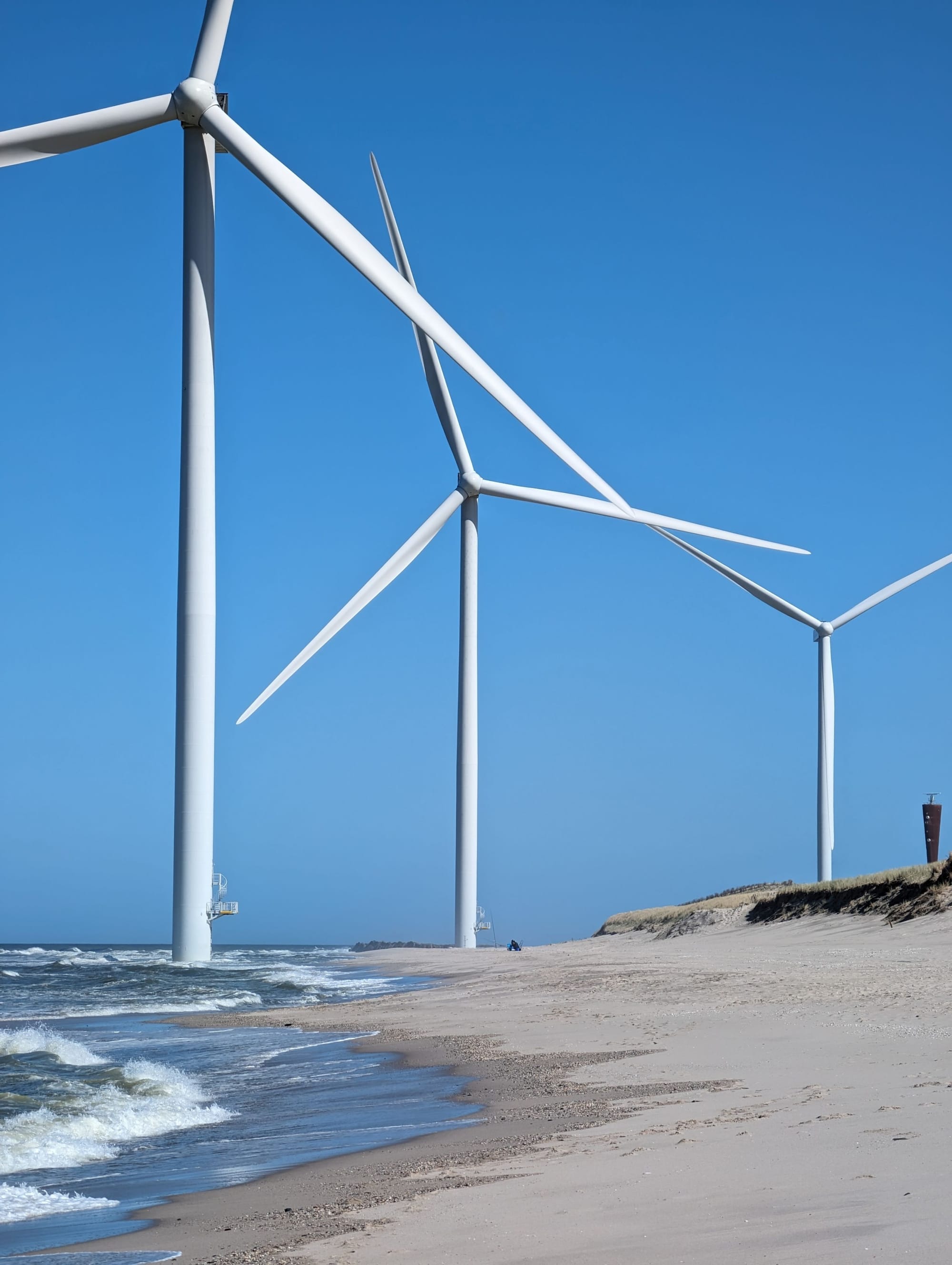 Windturbines langs de waterrand op de Maasvlakte bij Rotterdam, gezien vanuit een industrieel havengebied