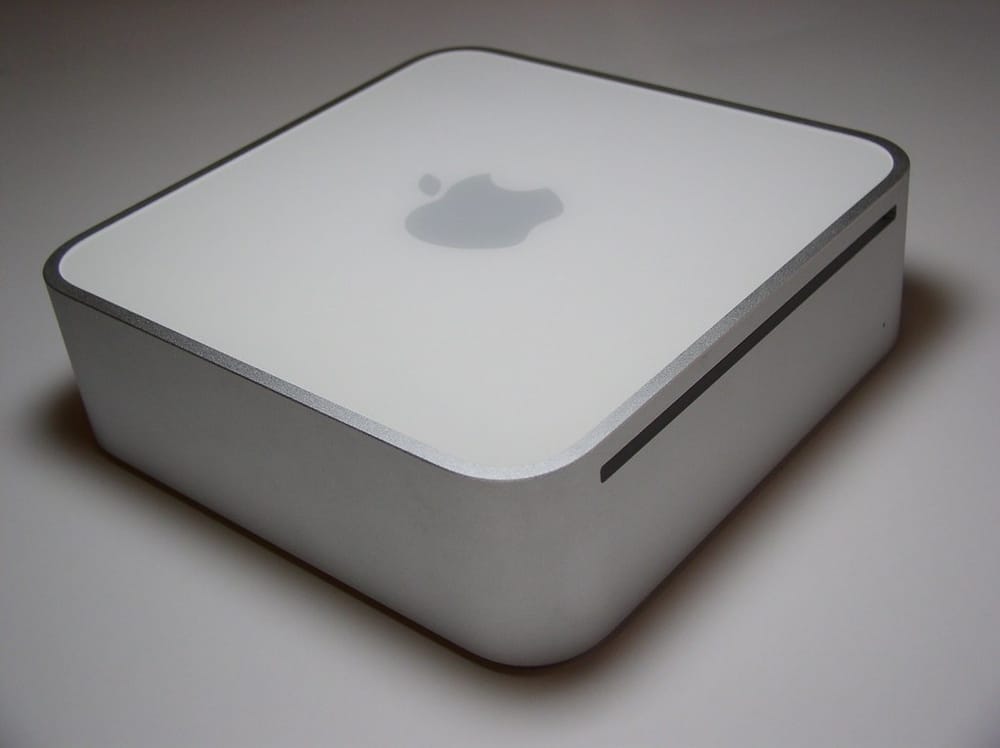 Apple Mac Mini in white aluminum housing photographed from the front-side angle on a light grey surface.