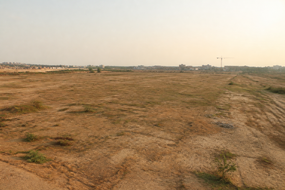 Vast empty dry plot of land under a hazy sky, with a distant construction crane on the horizon.