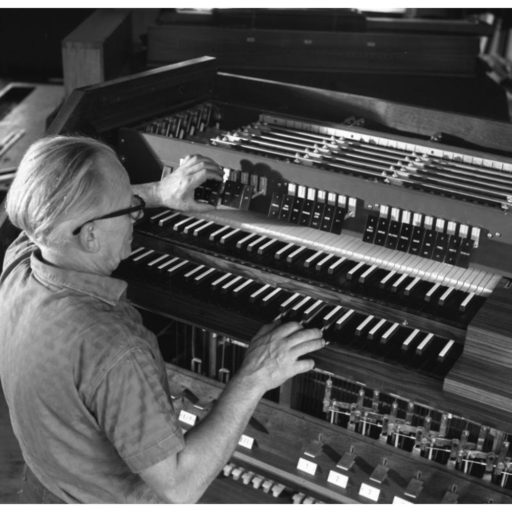 Archival black-and-white photo of a craftsman adjusting stops at an organ console in the Klais workshop.