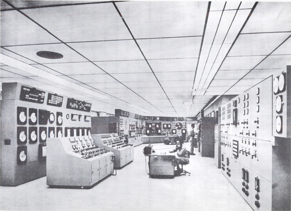 Historic electricity control room with instrument panels, desks and operators inside a large industrial interior.