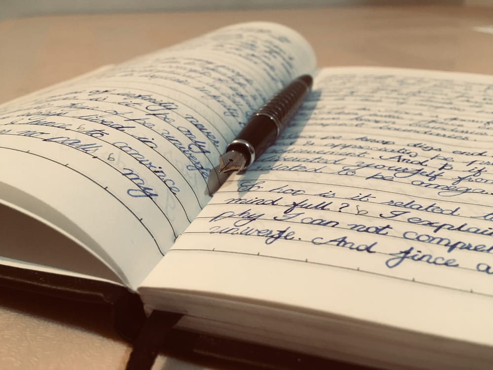 An open handwritten notebook with a fountain pen lying across the pages, viewed from a low angle.